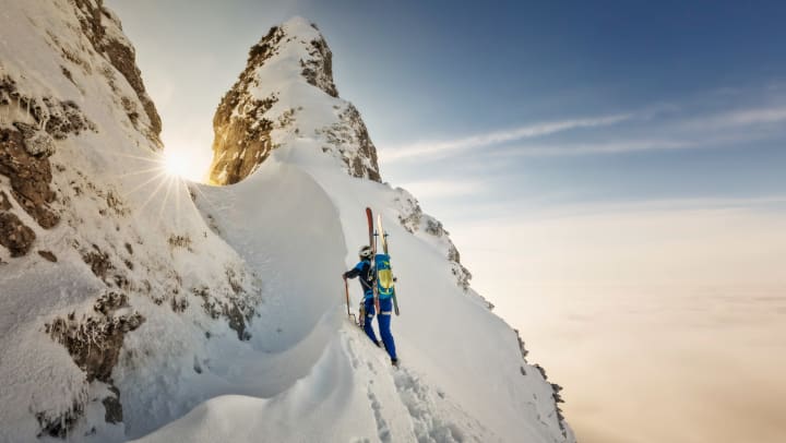 Climber scales snowy peak with skis in a backpack