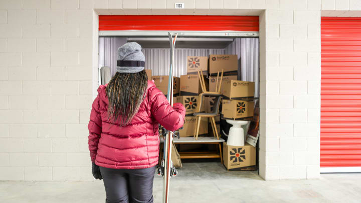 Woman holding skis with back to camera looking into a storage unit full of boxes