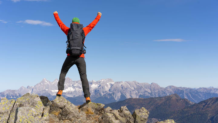 Person stands atop a rocky ridge with hands in the air while looking out over mountains