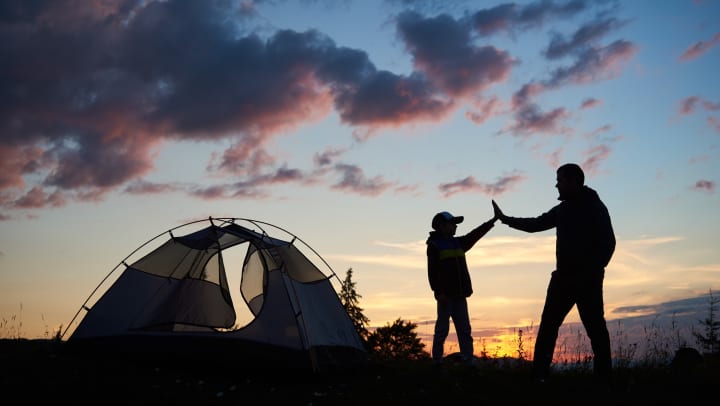 Two silhouetted people high-fiving next to a tent