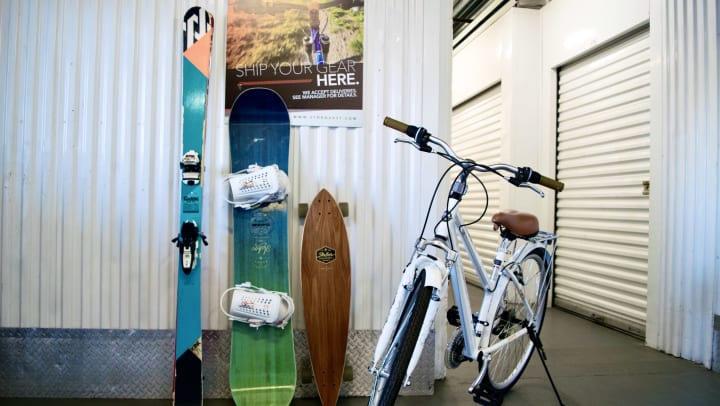 A pair of skis, a snowboard, a skateboard, and a bike in a storage facility hallway