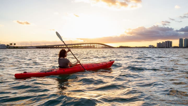 A person paddling a kayak in open water with a bridge in the distance