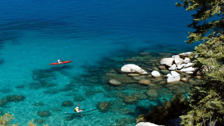 Two people sitting in kayaks paddling on water that is clear and blue.