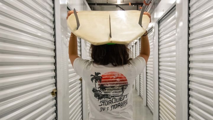 Person walks through a self storage corridor while holding a surfboard